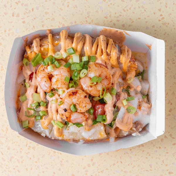 Loaded baked potato topped with shrimp, creamy sauce, and green onions in a white tray.