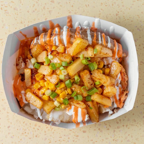 Baked potato topped with golden fries, corn, green onions, and drizzled with white and orange sauces.