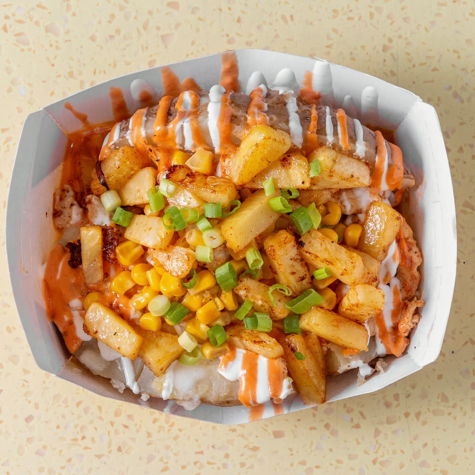 Baked potato topped with golden fries, corn, green onions, and drizzled with white and orange sauces.