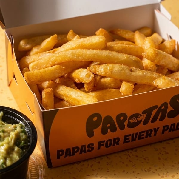 Golden french fries in an orange Papotas box with a side of guacamole.