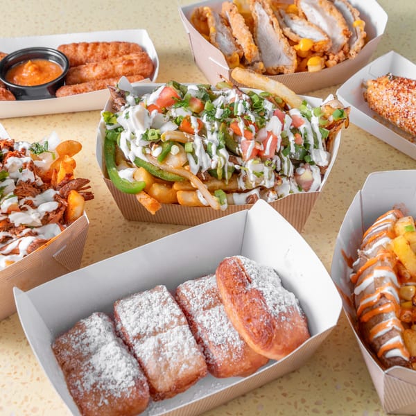 Multiple takeout containers filled with loaded fries, fried chicken, beignets, and elote.