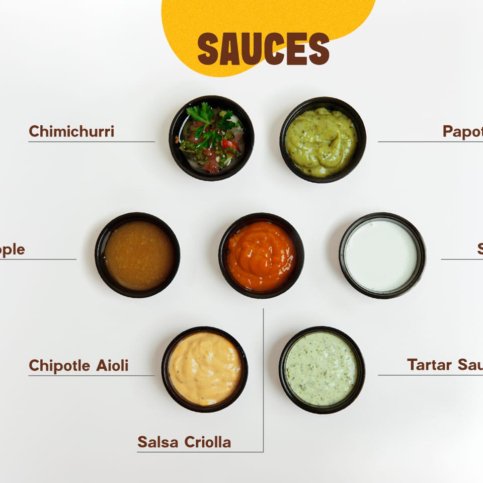 Assortment of seven labeled sauces in small black bowls, including chimichurri, sour cream, and aioli.